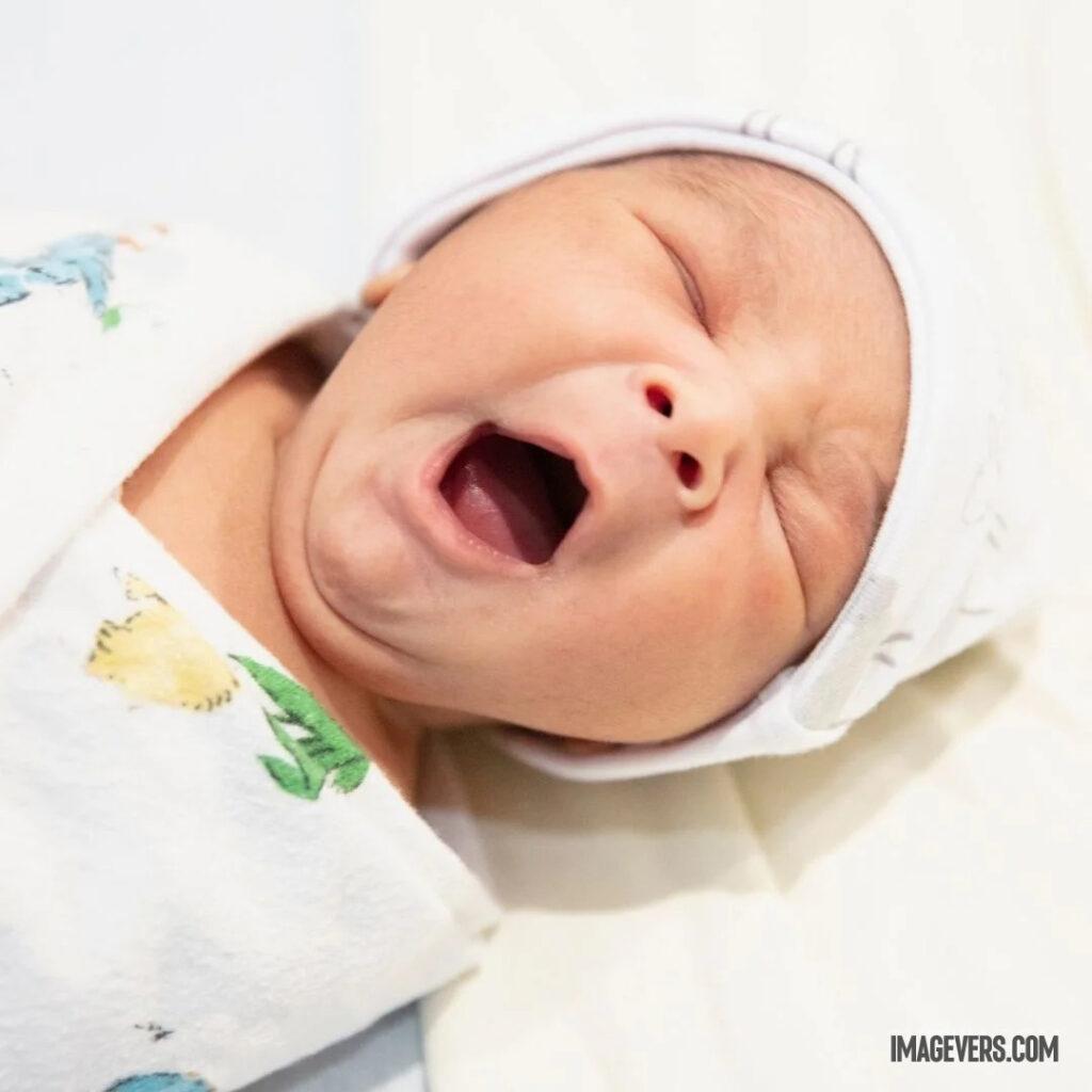 A newborn baby is sleeping on a white bed wearing white clothes and a cap and yawning wide open.jpg 2 11zon