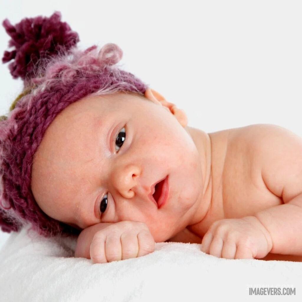A newborn baby is wearing a red purple hat on a white blanket and is lying with his head resting on his right arm.jpg 14 11zon
