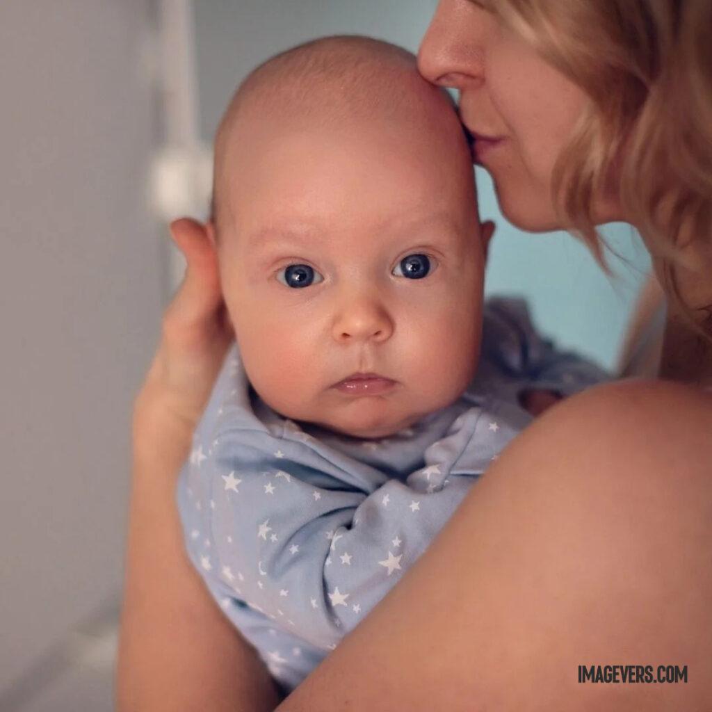 A newborn baby wearing a light blue cloth on his mothers lap is looking at someone in front and his mother is kissing his head.jpg 23 11zon
