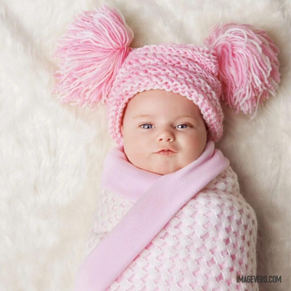 A newborn baby wearing a pinkish white robe and hat is looking up on a cream colored velvet bed.jpg 24 11zon