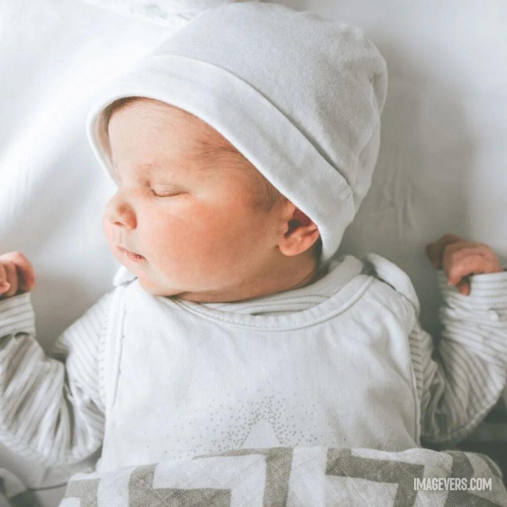 A newborn baby wearing a white robe and cap is sleeping soundly on a white bed with his face turned to the right.jpg 29 11zon