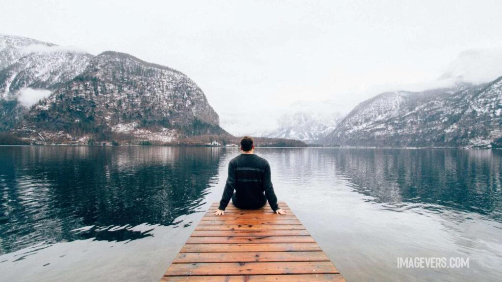 Man sitting on wooden aisle by the lake watching mountains